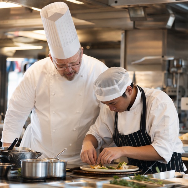 Commis chef prepping ingredients under a senior chef's supervision