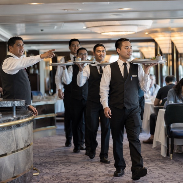 Head waiter directing a line of waiters carrying plated dishes through the dining room