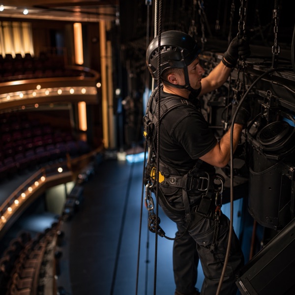 Rigger in a safety harness checking aerial equipment above a theatre stage